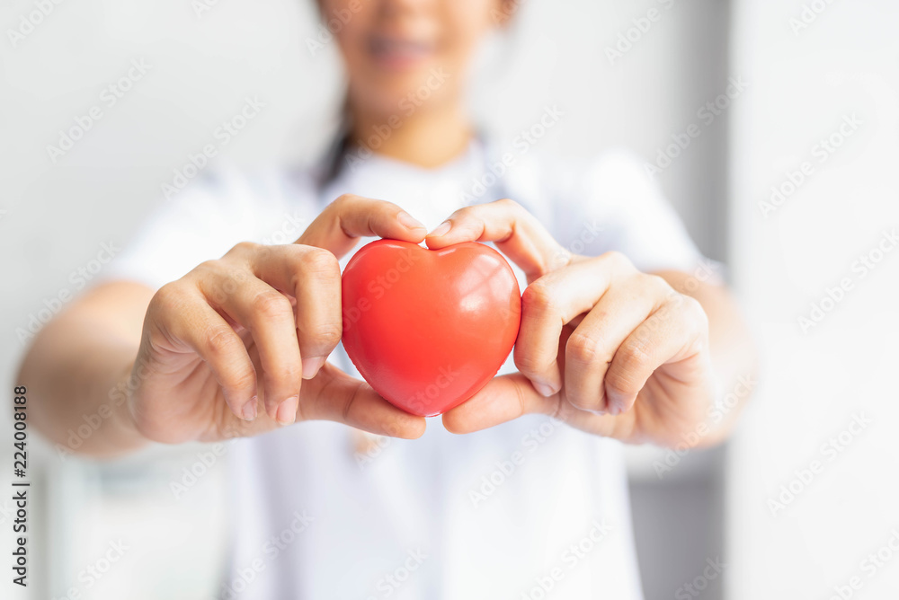 Selected focus on doctor with white uniform holding a red heart toward front side. Heart and healthh care conceptual. Selected focus on doctor with white uniform holding a red heart toward front side. Heart and healthh care conceptual.