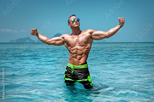 Athletic young sexy wet naked man posing in the ocean in board shorts
