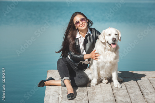 Young attractive woman sitting at the pier with her dog. Best friends outdoors