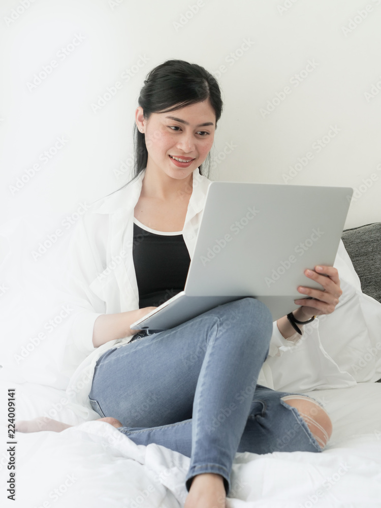 Happy Asian woman using laptop on bed, relaxing at home. Happy Asian woman using laptop on bed, relaxing at home.