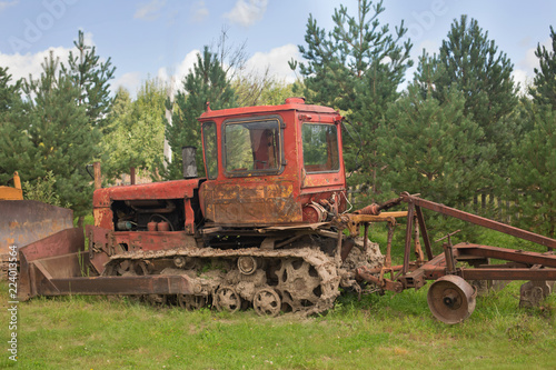 Old farm tractor in pines and fir trees before the fence