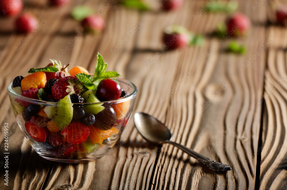 Assorted fruits in glass bowl on kitchen wooden table with spoon aside Assorted fruits in glass bowl on kitchen wooden table with spoon aside