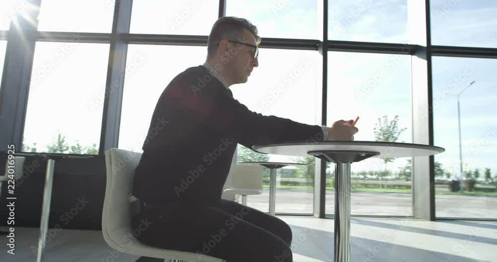 Mature man sitting in cafe of modern office building and using phone Mature man sitting in cafe of modern office building and using phone