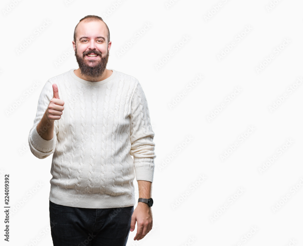 Young caucasian hipster man wearing winter sweater over isolated background doing happy thumbs up gesture with hand. Approving expression looking at the camera with showing success. Young caucasian hipster man wearing winter sweater over isolated background doing happy thumbs up gesture with hand. Approving expression looking at the camera with showing success.