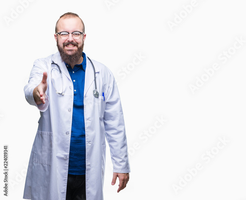 Young caucasian doctor man wearing medical white coat over isolated background smiling friendly offering handshake as greeting and welcoming. Successful business.