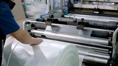 worker in the production of plastic packaging removes the roll with the finished product