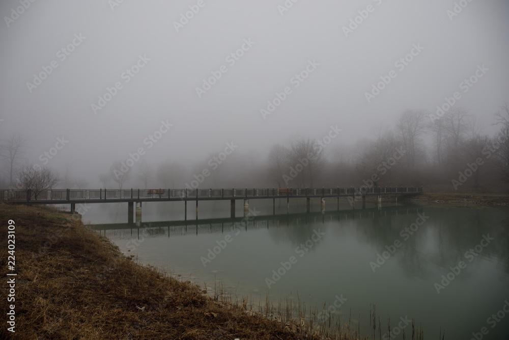 Amazing landscape of bridge reflect on surface water of lake, fog evaporate from pond make romantic scene or Beautiful bridge on lake with trees at fog.