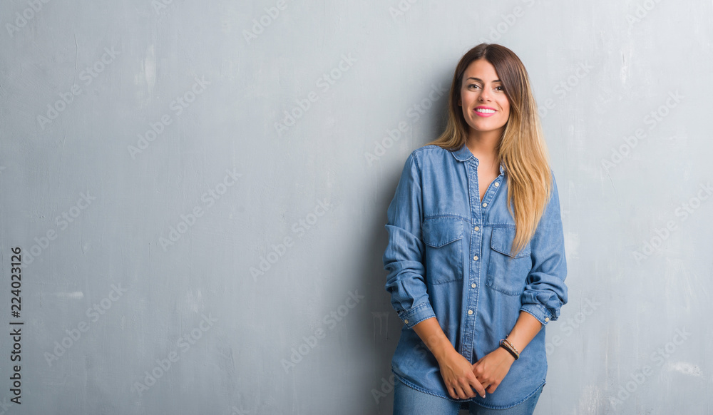 Young adult woman over grunge grey wall wearing denim outfit with a happy and cool smile on face. Lucky person. Young adult woman over grunge grey wall wearing denim outfit with a happy and cool smile on face. Lucky person.