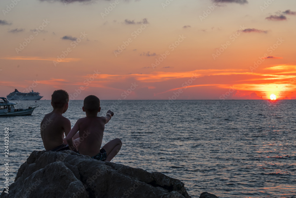 Silhouette of a two boys pointing to the sun over the sea. Evening landscape. Silhouette of a two boys pointing to the sun over the sea. Evening landscape.