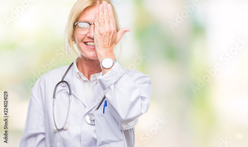 Middle age blonde doctor woman over isolated background covering one eye with hand with confident smile on face and surprise emotion.