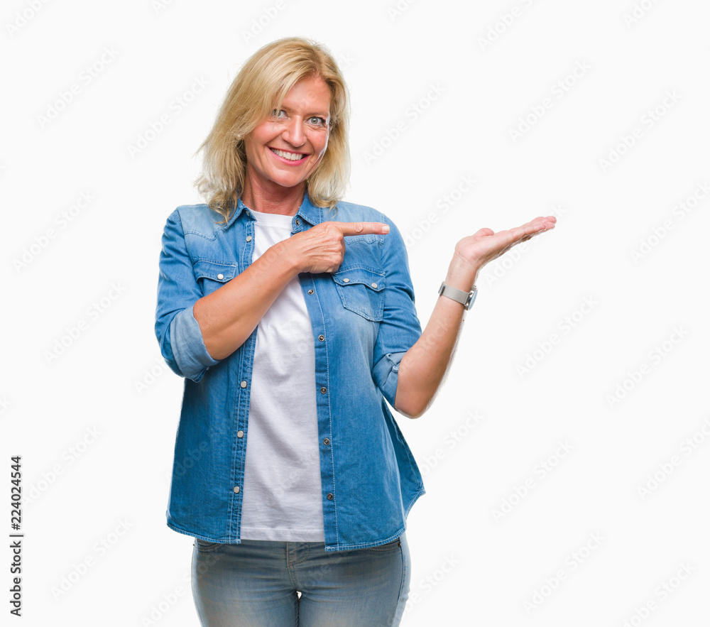 Middle age blonde woman over isolated background amazed and smiling to the camera while presenting with hand and pointing with finger. Middle age blonde woman over isolated background amazed and smiling to the camera while presenting with hand and pointing with finger.
