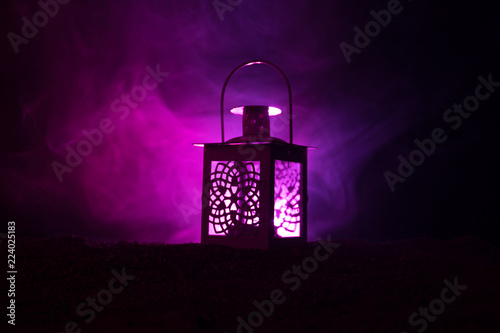 Ornamental Arabic lantern with burning candle glowing at night on dark toned foggy background. Festive greeting card, invitation for Muslim holy month Ramadan Kareem.