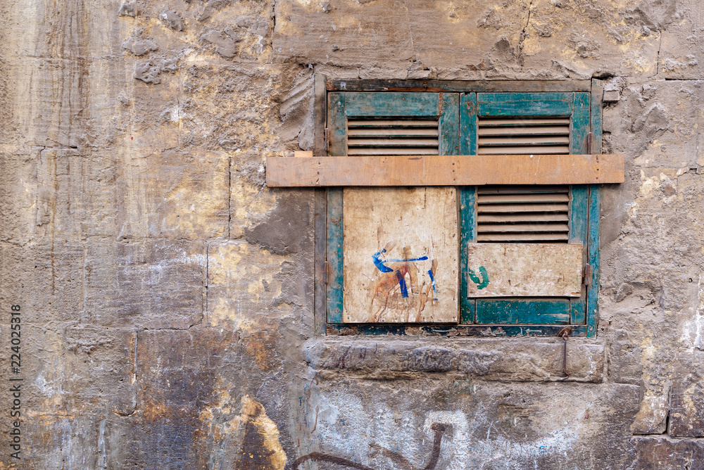 Old grunge window with closed green broken shutters on dirty cracked bricks stone wall Old grunge window with closed green broken shutters on dirty cracked bricks stone wall