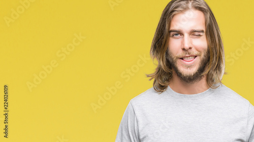 Young handsome man with long hair over isolated background winking looking at the camera with sexy expression, cheerful and happy face.