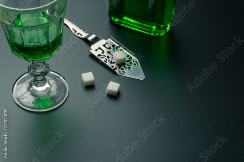 a glass of absinthe, a stainless steel slotted spoon with the sugar cubes and the absinthe bottle on the table photo