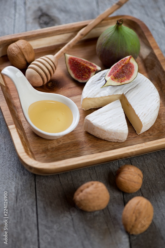 Camembert cheese with fig fruits, honey and walnuts on wooden serving tray, vertical shot, close-up