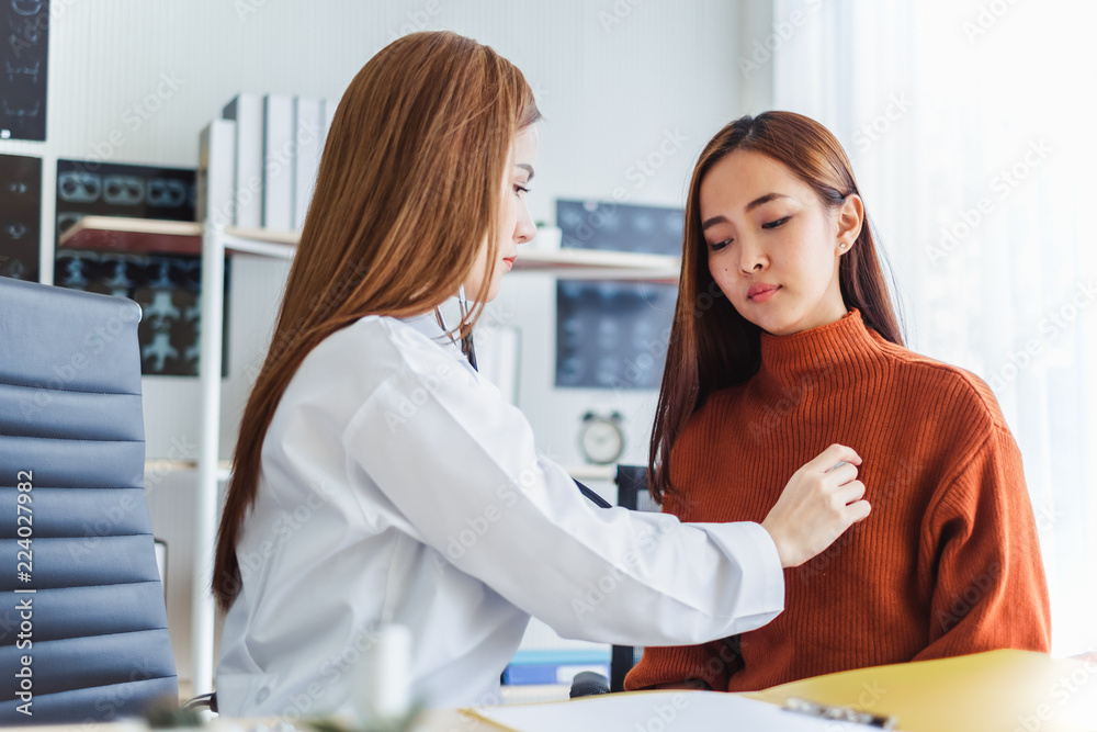 Asian doctor examining young asian patient by using stethoscope at her chest Asian doctor examining young asian patient by using stethoscope at her chest