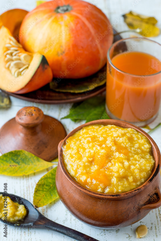 Φωτογραφία A small clay pot with millet porridge, a glass with natural freshly prepared juice and a fresh ripe pumpkin on an old wooden table