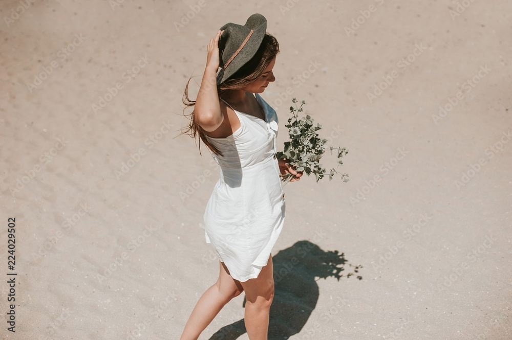 Φωτογραφία Beautiful young hipster girl enjoying a sunny beautiful day walking along the beach picking wild plants and looking happy