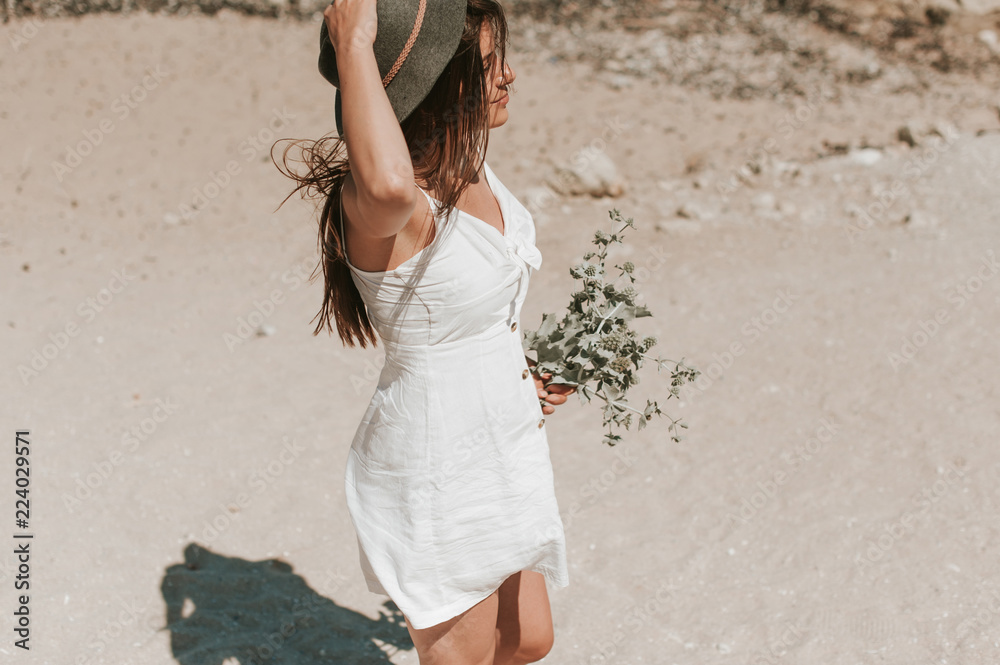 Φωτογραφία Beautiful young hipster girl enjoying a sunny beautiful day walking along the beach picking wild plants and looking happy