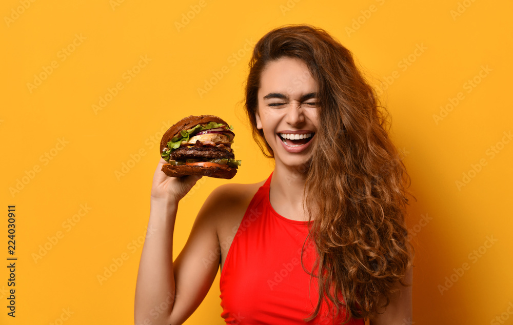 Woman hold big barbecue burger sandwich with hungry mouth happy screaming laughing on yellow background