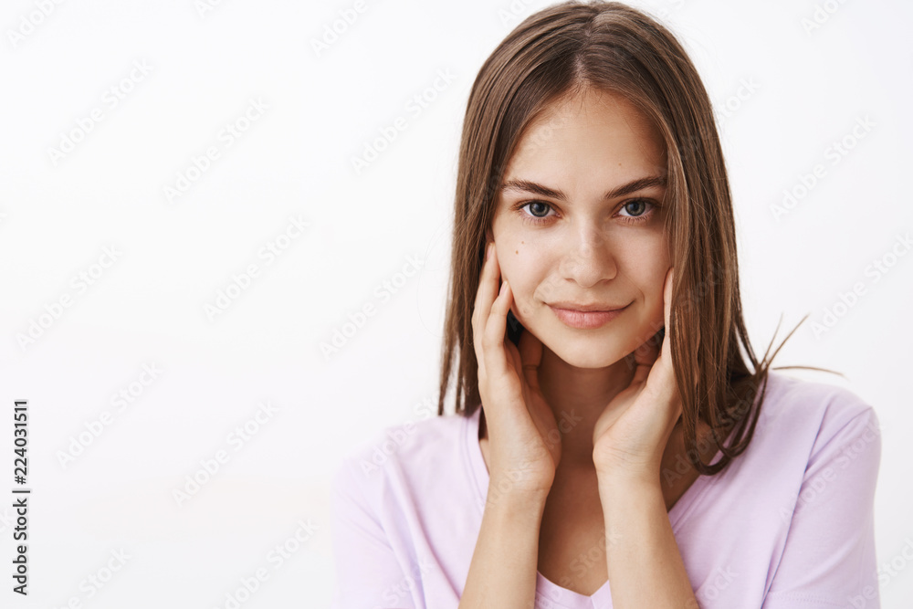 She knows how attract men attention. Confident feminine attractive female brunette with straight hair and clean skin touching face gently and smiling daring at camera flirting over white wall She knows how attract men attention. Confident feminine attractive female brunette with straight hair and clean skin touching face gently and smiling daring at camera flirting over white wall