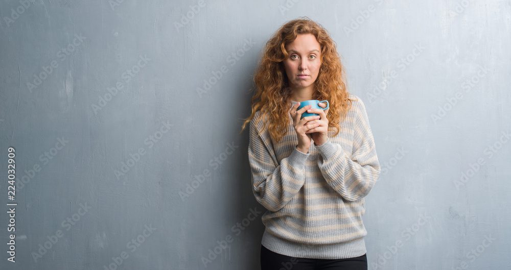 Young redhead woman over grey grunge wall drinking a cup of coffee with a confident expression on smart face thinking serious Young redhead woman over grey grunge wall drinking a cup of coffee with a confident expression on smart face thinking serious