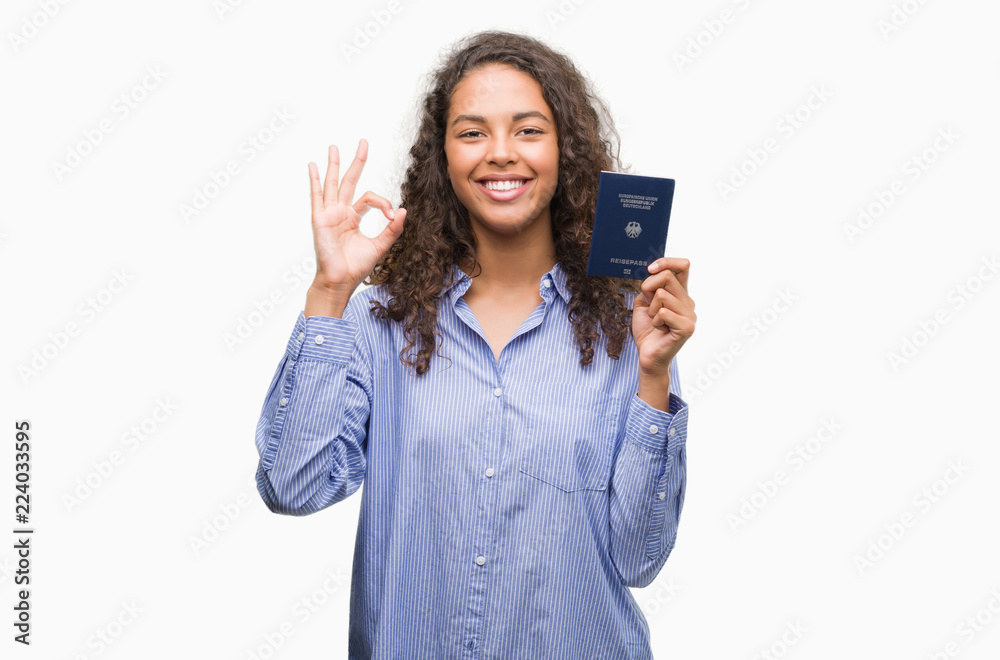 Young hispanic woman holding passport of Germany doing ok sign with fingers, excellent symbol