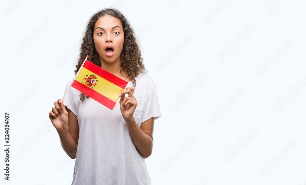 Young hispanic woman holding flag of Spain scared in shock with a surprise face, afraid and excited with fear expression Young hispanic woman holding flag of Spain scared in shock with a surprise face, afraid and excited with fear expression