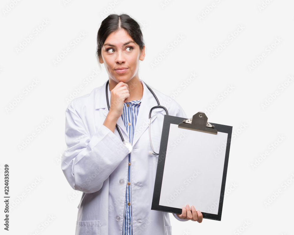 Young hispanic doctor woman holding clipboard serious face thinking about question, very confused idea Young hispanic doctor woman holding clipboard serious face thinking about question, very confused idea