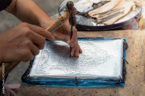 The artisans are using hammers and steel Engraved gorgeus pattern on silver plate To handcraft concept.