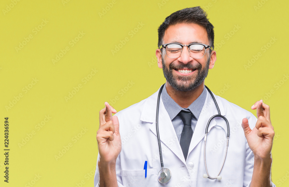 Adult hispanic doctor man over isolated background smiling crossing fingers with hope and eyes closed. Luck and superstitious concept. Adult hispanic doctor man over isolated background smiling crossing fingers with hope and eyes closed. Luck and superstitious concept.