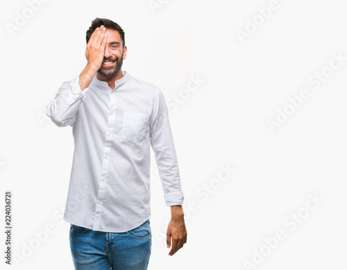 Adult hispanic man over isolated background covering one eye with hand with confident smile on face and surprise emotion. © Krakenimages.com