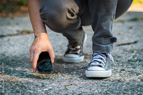 Woman lifting up cracked smartphone from the ground