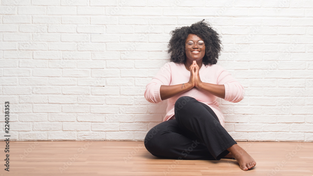 Young african american woman sitting on the floor at home praying with hands together asking for forgiveness smiling confident. Young african american woman sitting on the floor at home praying with hands together asking for forgiveness smiling confident.