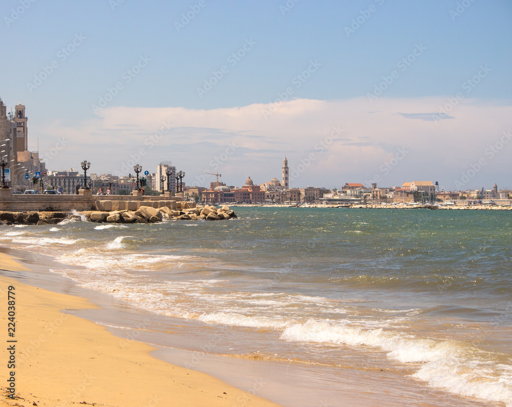 Bari, Italy - 06/16/2018: Sand beach of Mediterranean sea with city panorama of Bari. Coastline with waves and embankment. Holiday and vacation concept. Bari cityscape. 