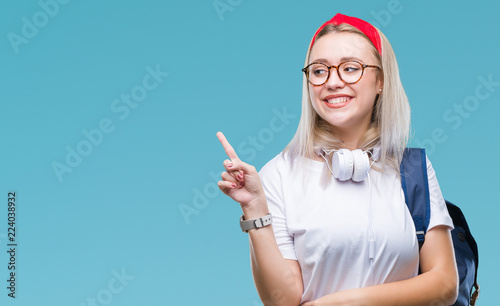 Young blonde student woman wearing glasses and backpack over isolated background with a big smile on face  pointing with hand and finger to the side looking at the camera.
