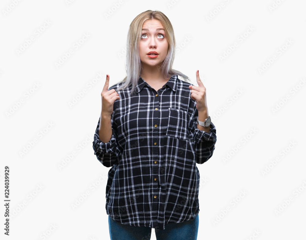 Young blonde woman over isolated background amazed and surprised looking up and pointing with fingers and raised arms. Young blonde woman over isolated background amazed and surprised looking up and pointing with fingers and raised arms.