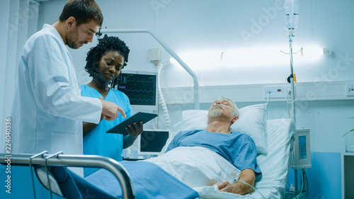 In the Hospital, Senior Man Sleeps in the Bed, Doctor and Nurse Standing in the Ward, Using Tablet Computer. Technology Helps Cure Patients, Modern Hospital Ward.