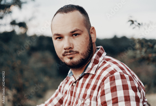 Portrait of a beautiful bearded young man in a checkered shirt, photographed in nature