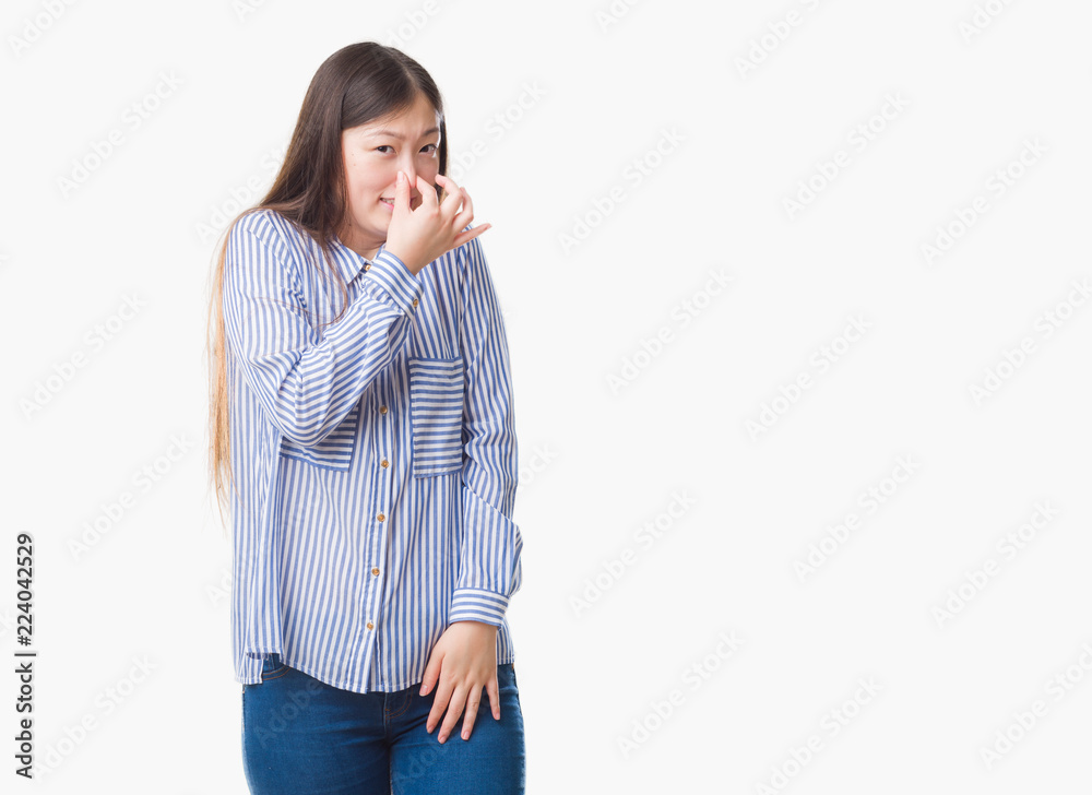 Young Chinese woman over isolated background smelling something stinky and disgusting, intolerable smell, holding breath with fingers on nose. Bad smells concept. Young Chinese woman over isolated background smelling something stinky and disgusting, intolerable smell, holding breath with fingers on nose. Bad smells concept.