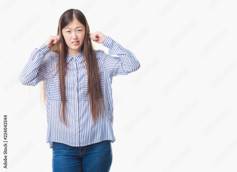 Young Chinese woman over isolated background covering ears with fingers with annoyed expression for the noise of loud music. Deaf concept. Young Chinese woman over isolated background covering ears with fingers with annoyed expression for the noise of loud music. Deaf concept.