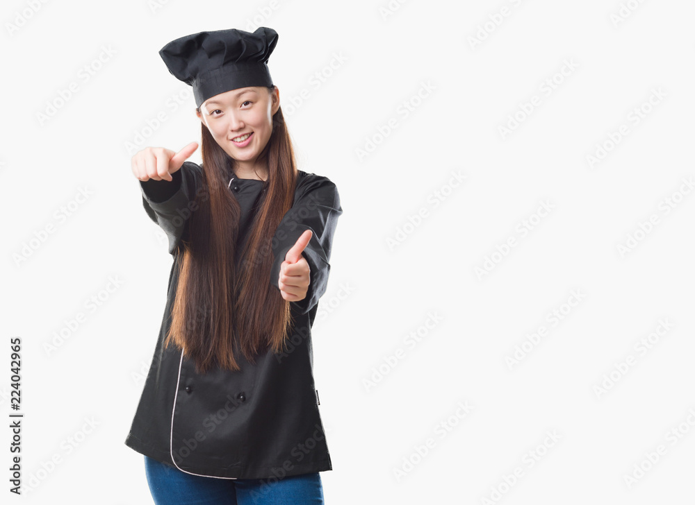 Young Chinese woman over isolated background wearing chef uniform approving doing positive gesture with hand, thumbs up smiling and happy for success. Looking at the camera, winner gesture. Young Chinese woman over isolated background wearing chef uniform approving doing positive gesture with hand, thumbs up smiling and happy for success. Looking at the camera, winner gesture.