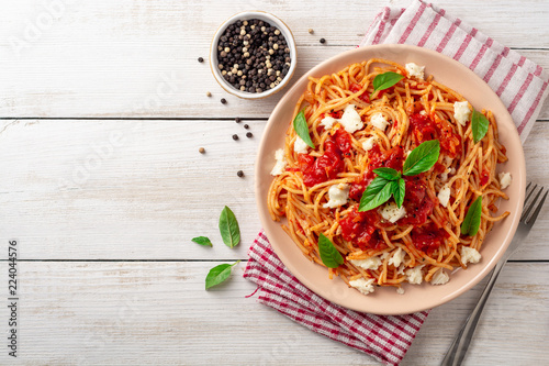 Spaghetti pasta with tomato sauce, mozzarella cheese and fresh basil in plate on white wooden background. Top view. Copy space.