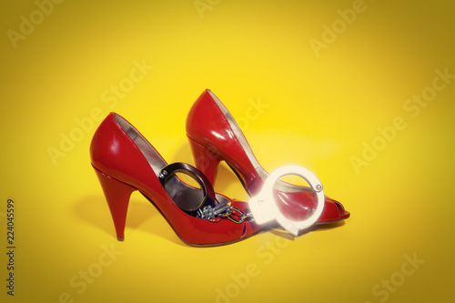 A pair of shiny metal handcuffs over red leather shoes. Symbolic shot: fetish, sexuality, mistress, constraint, pleasure. With vignette.
