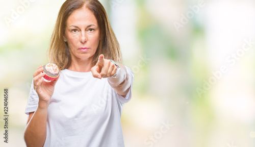 Middle age hispanic woman eating cupcake over isolated background pointing with finger to the camera and to you, hand sign, positive and confident gesture from the front