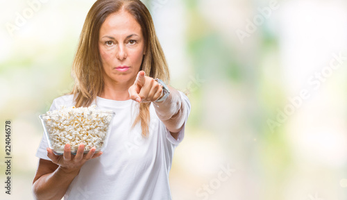 Middle age hispanic woman eating popcorn over isolated background pointing with finger to the camera and to you  hand sign  positive and confident gesture from the front