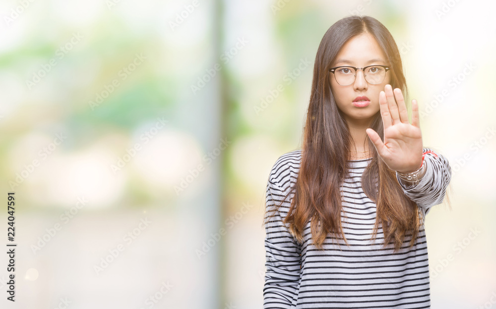 Young asian woman wearing glasses over isolated background doing stop sing with palm of the hand. Warning expression with negative and serious gesture on the face.