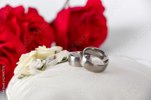 wedding rings - wedding rings on a white silk pillow with red roses in the background