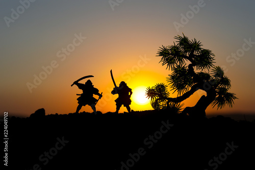 Silhouette of two samurais in duel. Picture with two samurais and sunset sky. Selective focus